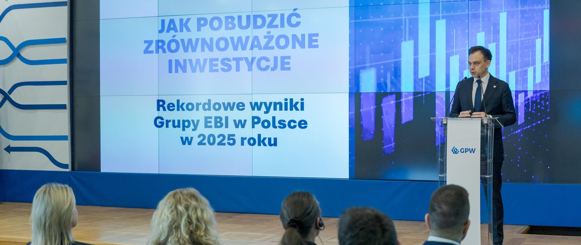 Minister finansów i gospodarki Andrzej Domański podczas konferencji, na ekranie widoczny jest slajd o pobudzaniu zrównoważonych inwestycji i wynikach Grupy EBI w Polsce.