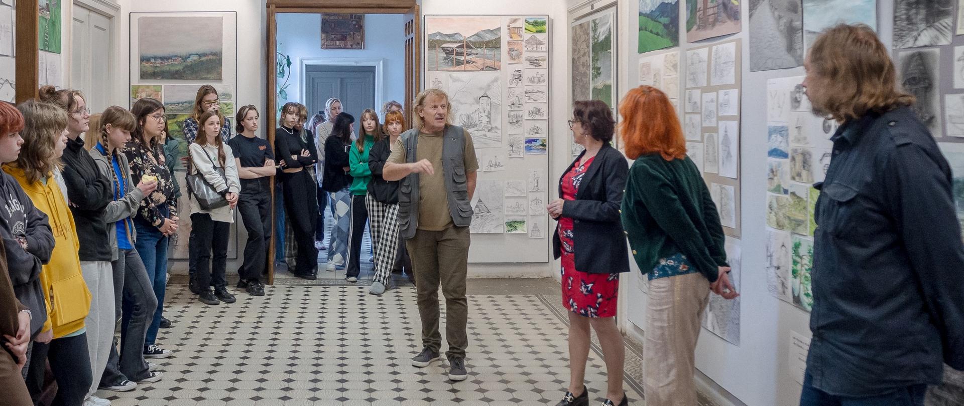 Hol szkolny z pracami rysunkowymi i malarskimi oraz grupą osób