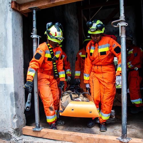 Kobieta i mężczyzna w strojach strażaków wynoszą rannego na noszach