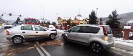 Zdjęcie przedstawia dwa samochody osobowe po zderzeniu czołowym, w tle widać budynek Komendy Powiatowej Państwowej Staży Pożarnej w Suchej Beskidzkiej 