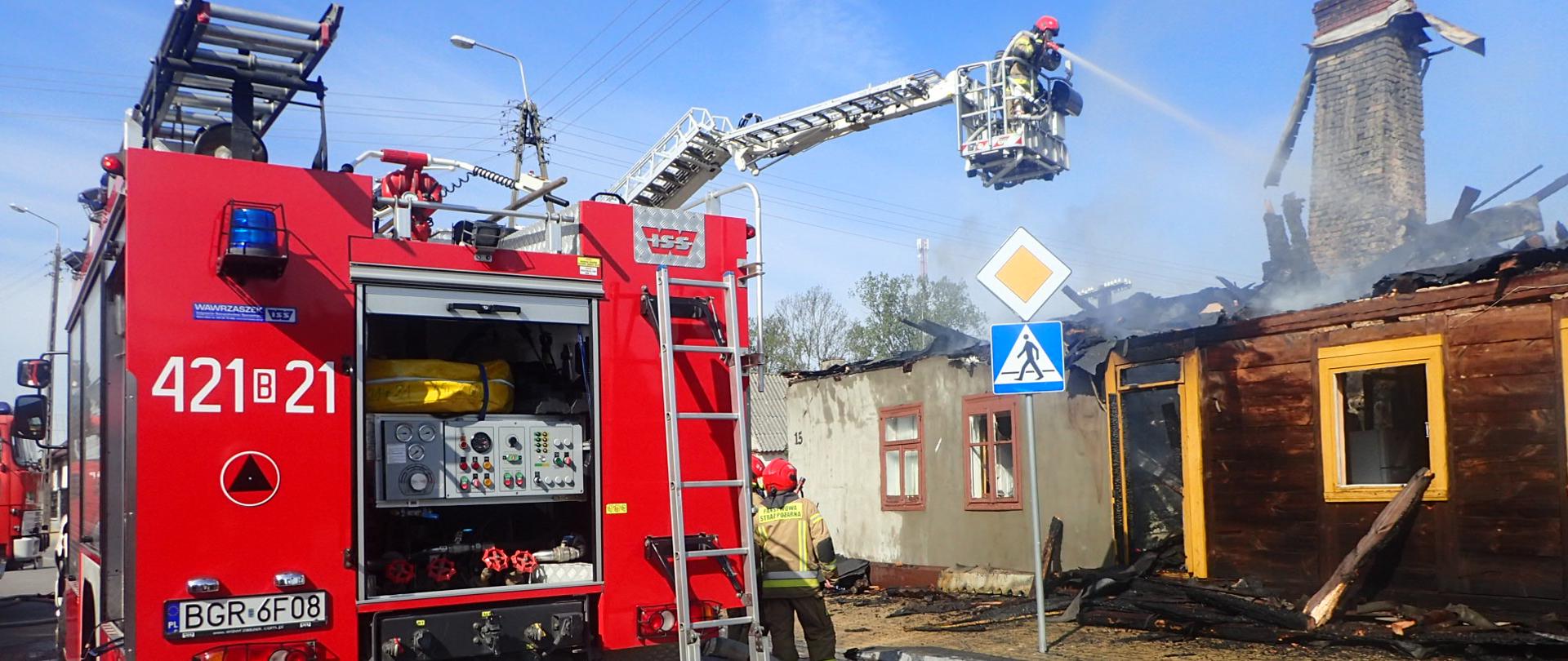 Samochód gaśniczy a w tle kosz SHD ze strażakami gaszącymi pożar.