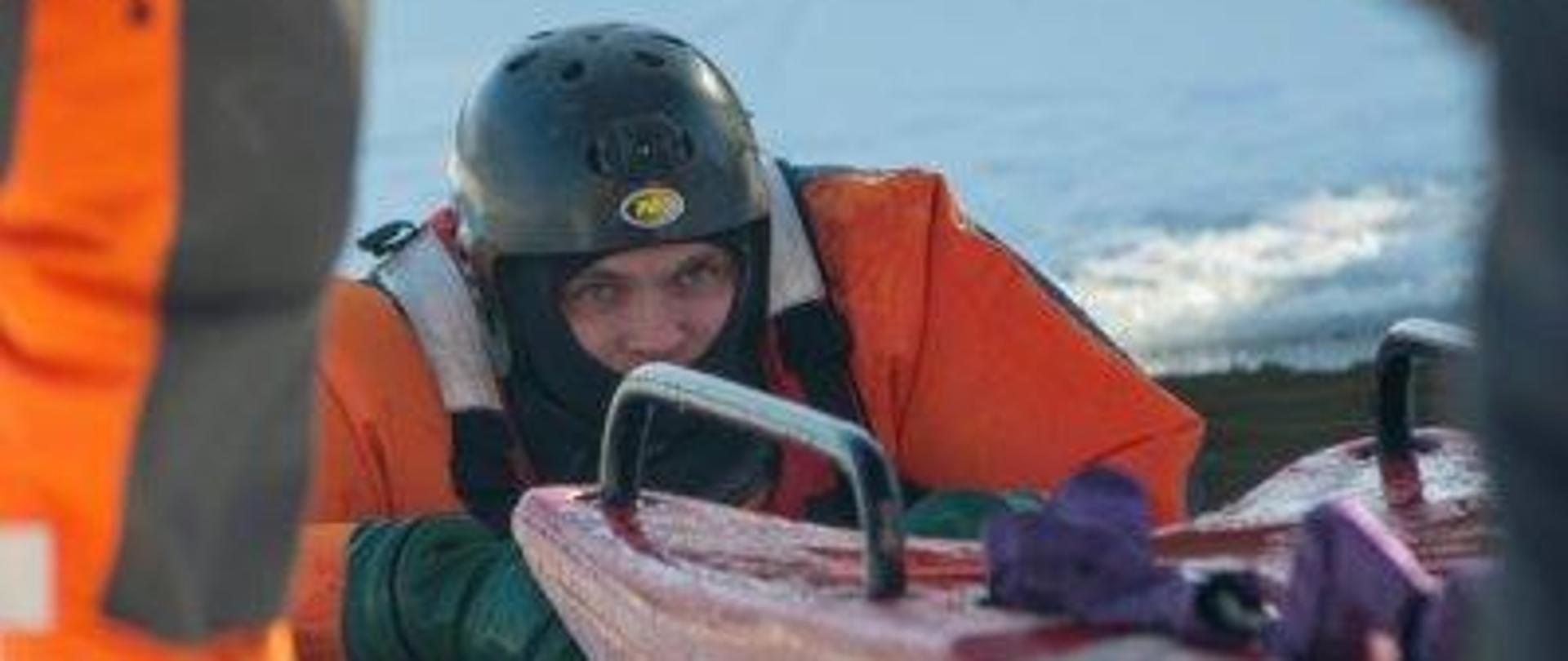 Zdjęcie przedstawia ratownika zanurzonego częściowo w przeręblu. Sanie lodowe będą służyć do jego ewakuacji.
