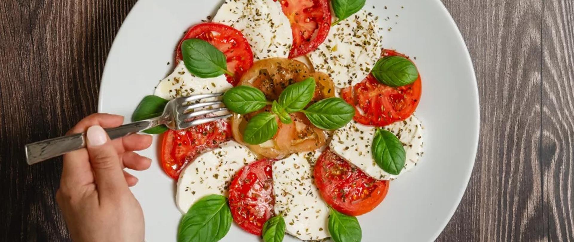 Na zdjęciu są dwa główne napisy o treści : lokalna produkcja? twój wybór, Bezpieczeństwo? nasz priorytet oraz widać talerz na którym są ułożone pomidor ser mozzarella bazylia i przyprawy 