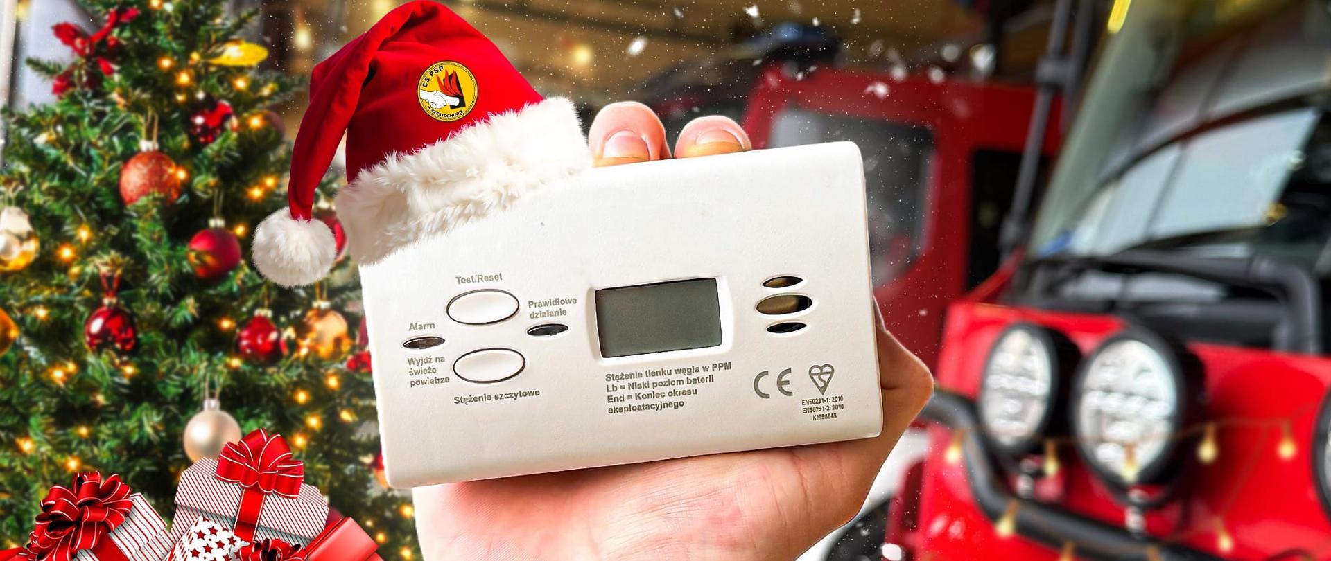 Grafika mikołajkowa. Na górze biały napis na czerwonym tle "Nie wiesz co kupić na Mikołajki" po prawej stronie napisu kolorowe logo Centralnej Szkoły PSP. Poniżej widoczna dłoń która trzyma białą czujkę czadu "ubraną" w czerwoną czapkę z białym futerkowym otokiem i pomponem, tło stanowi wnętrze garażu jednostki ratowniczo-gaśniczej z umieszczoną po lewej stronie choinką i prezentami dołożonymi dzięki programowi graficznemu