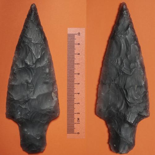 fotografia przedstawia krzemienny grot na pomarańczowym tle