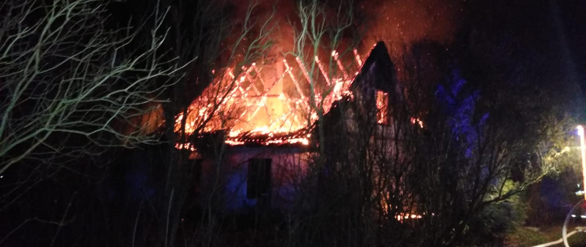 Zdjęcie zrobione nocą. Konstrukcja dachu budynku w ogniu, iskry i płomienie.