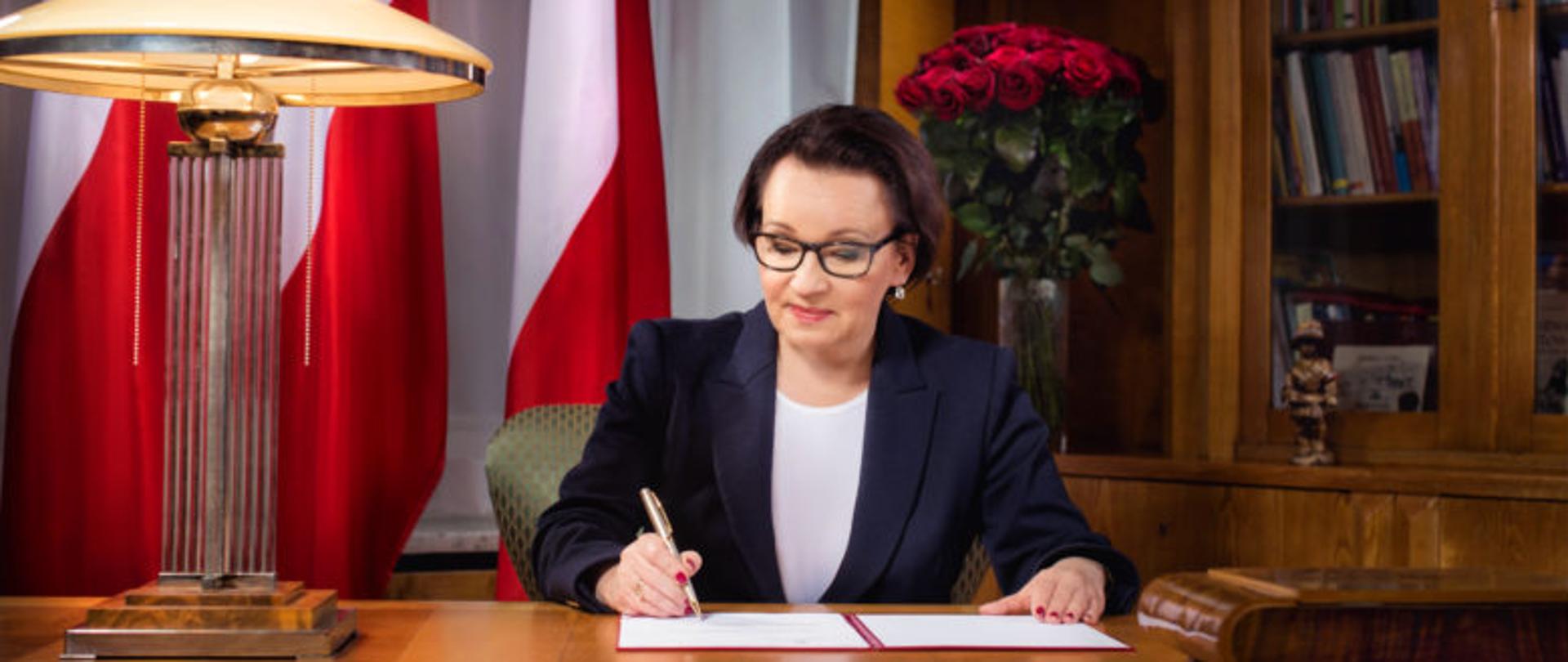 Minister Anna Zalewska podpisuje list przy biurku