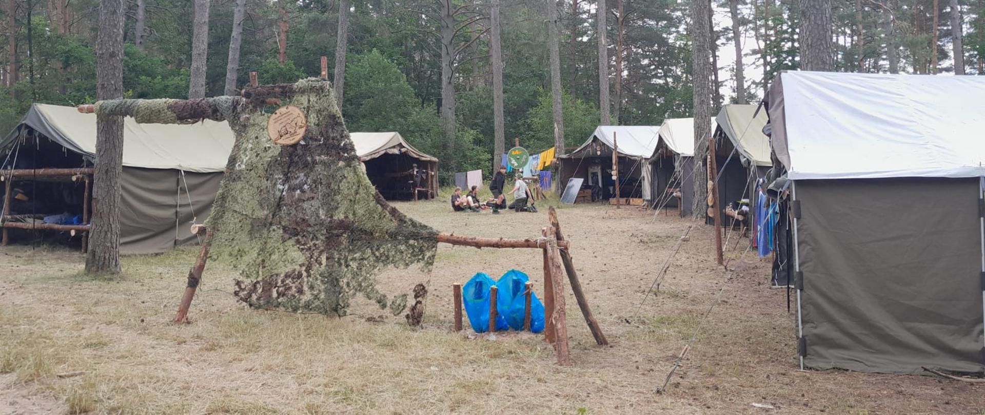 Obozowisko harcerskie na obszarze leśnym. Na środku siedzący w kręgu harcerze.