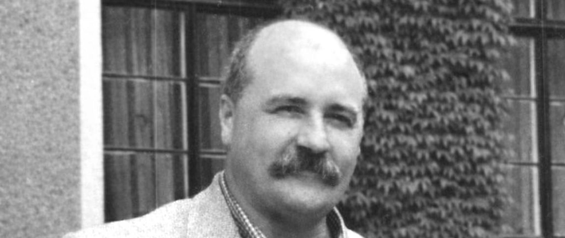 Zdjęcie przedstawia nauczyciela Piotra Lenartowicza stojącego przed szkołą.