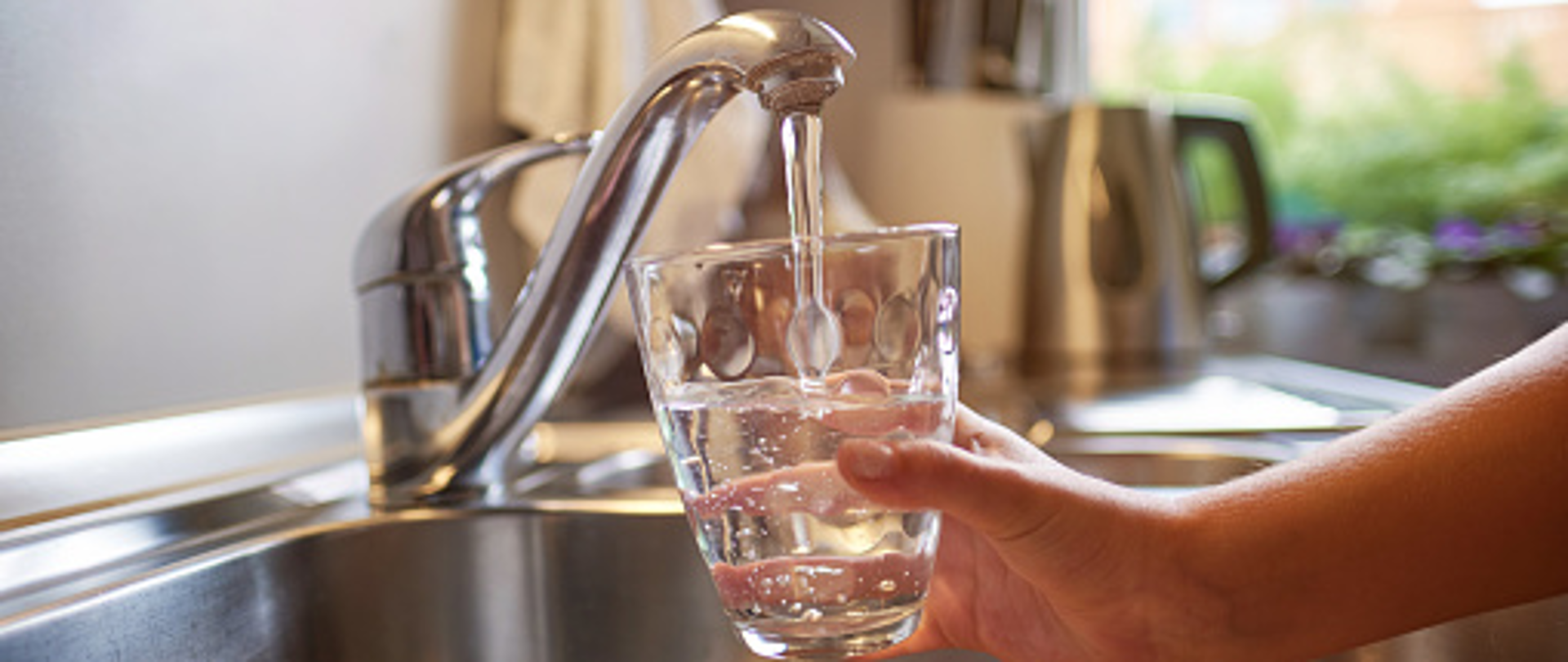 ręka trzymająca szklankę pod kranem z wodą