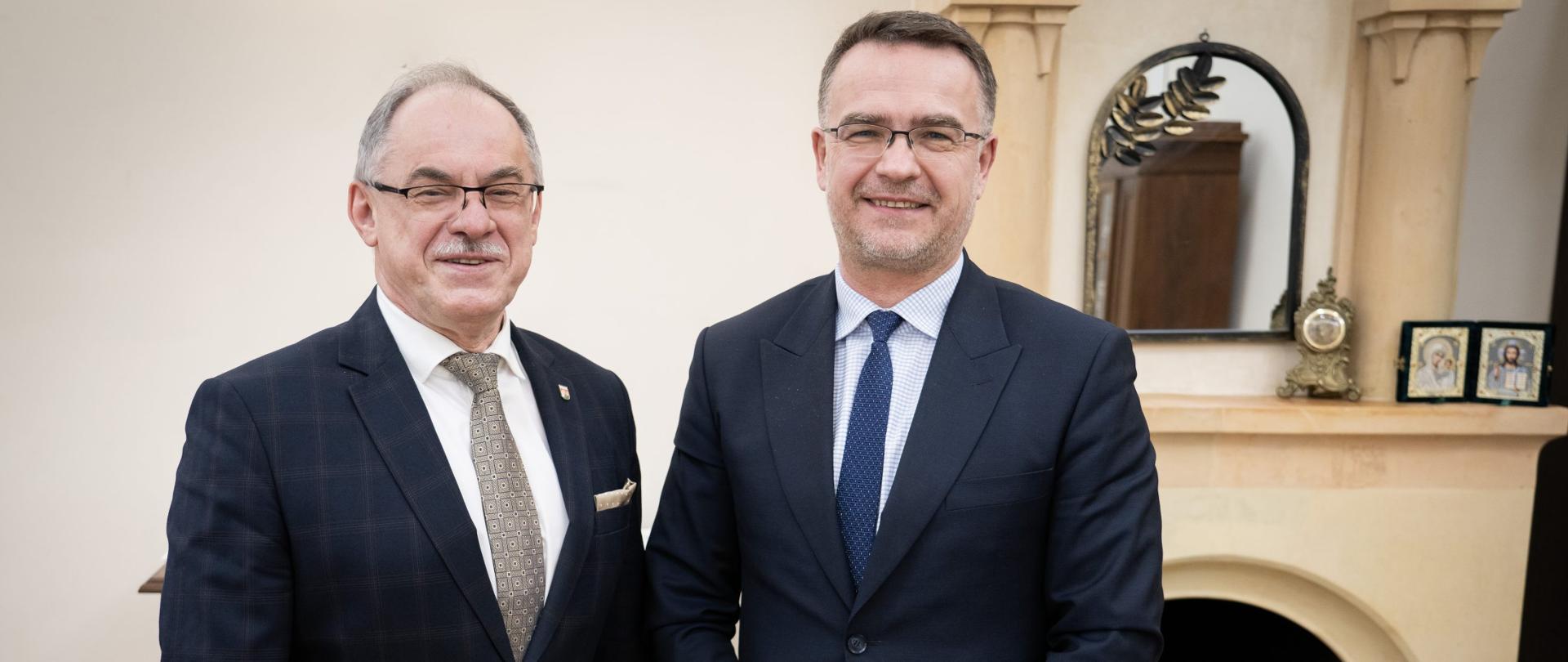 Adam Musiuk, Podlaski Wojewódzki Konserwator Zabytków, Czesław Renkiewicz, Prezydent Miasta Suwałk. Obaj mężczyźni ubrani w garnitury na tle kominka.