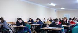 uczestnicy konkursu siedzą w ławkach na sali szkolnej i rozwiązują pisemny test