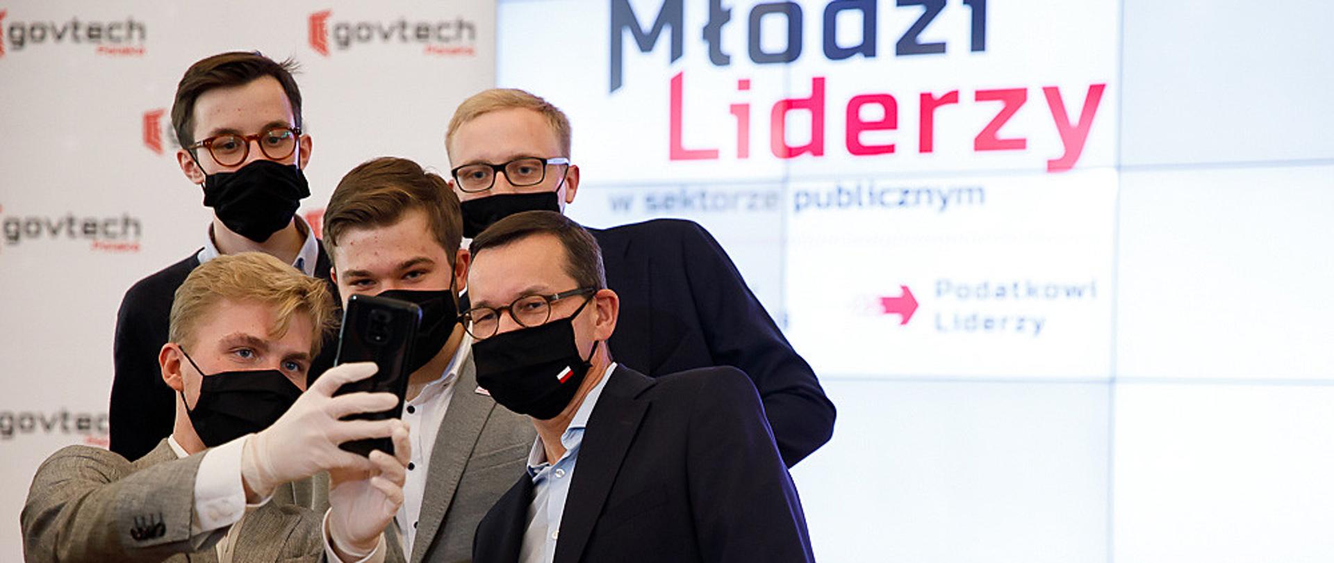 Premier Mateusz Morawiecki podczas spotkania z młodzieżą na tle baneru Młodzi Liderzy