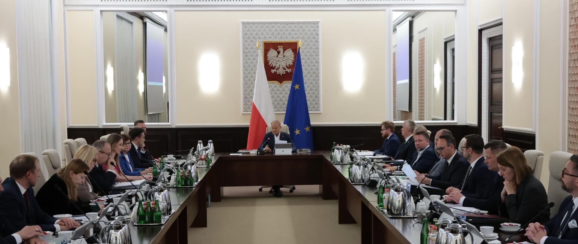 Grupa osób siedzi przy stołach na sali. Wśród nich jest minister Katarzyna Pełczyńska-Nałęcz.