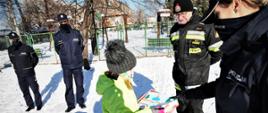 Na zdjęciu dziewczynka przekazuje rysunek policjantce, obok brygadier Wacław Pasterczyk oraz dwóch funkcjonariuszy policji, sceneria zimowa.
