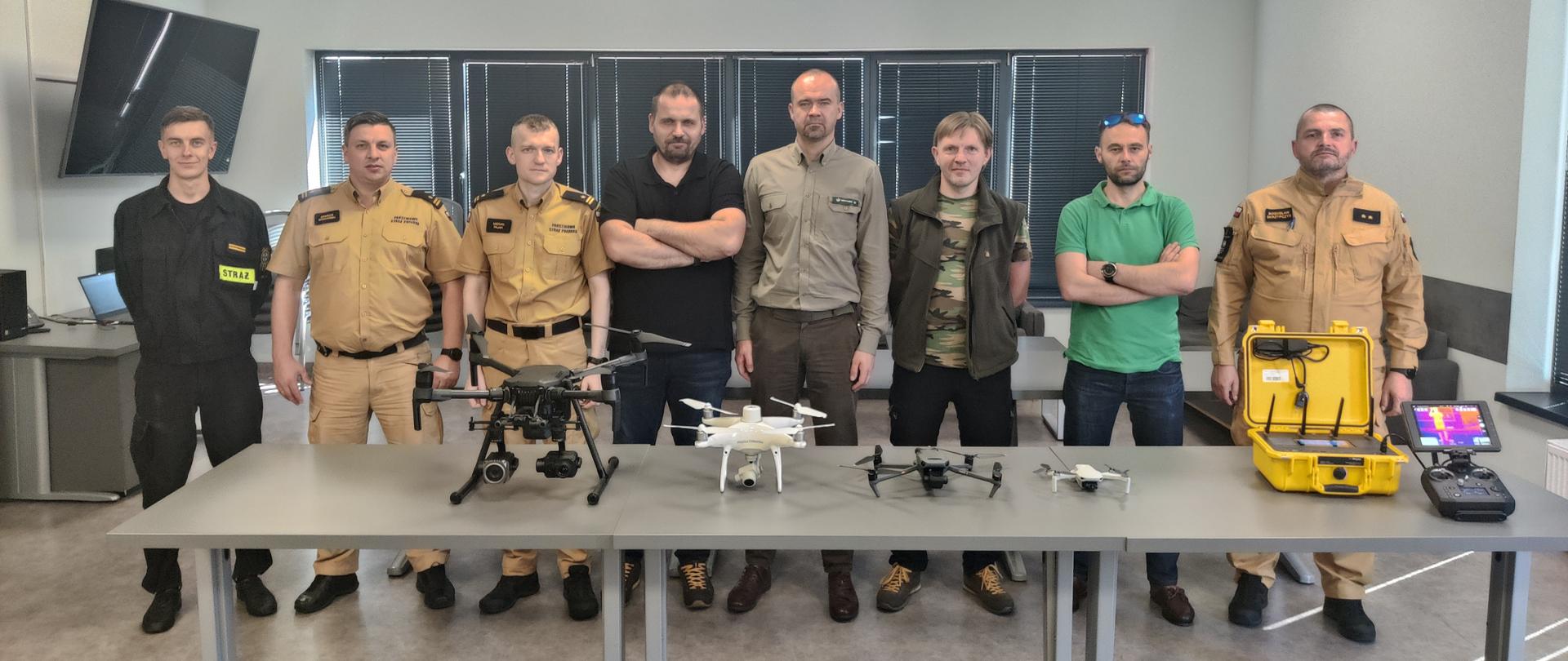 Na zdjęciu widzimy uczestników spotkania dotyczącego bezzałogowych statków powietrznych. Pozują do zdjęcia a przed nimi na stole w sali leżą drony.