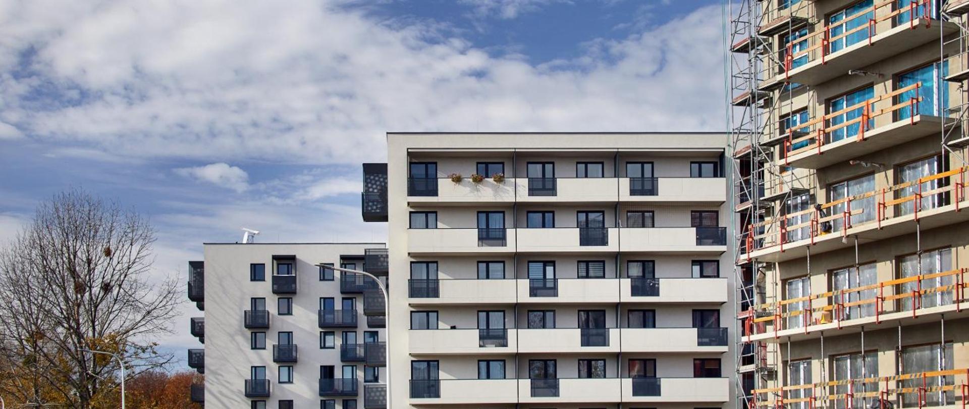 Na zdjęciu widać 2 nowo-wybudowane budynki oraz 1 w budowie. Świeci słońce. 