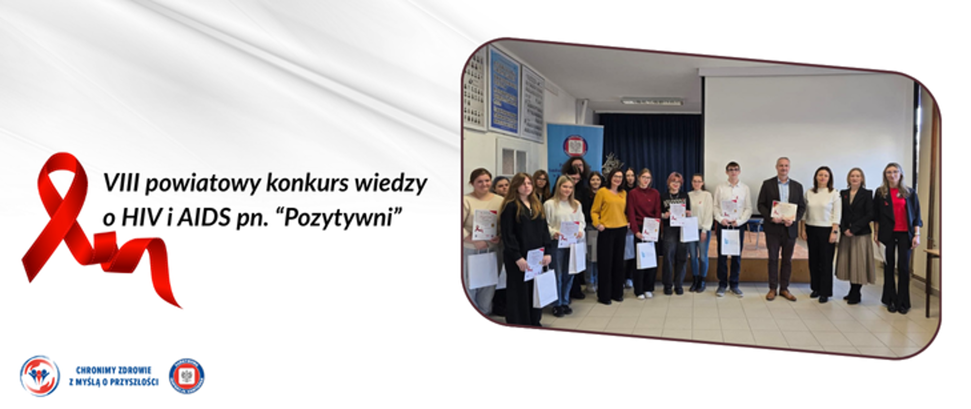 Grafika przedstawia czerwoną wstążkę, która jest symbolem HIV, a obok napis VIII powiatowy konkurs wiedzy o HIV i AIDS pn. "Pozytywni" na białym tle. Po prawej stronie w ramce znajduje się zdjęcie grupowe uczestników konkursu, opiekunów oraz przedstawicieli Starostwa Powiatowego w Kamieniu Pomorskim oraz Inspekcji Sanitarnej w Kamieniu Pomorskim. W lewym dolnym rogu umieszczono 2 logo Inspekcji Sanitarnej oraz hasło chronimy zdrowie z myślą o przyszłości. 
