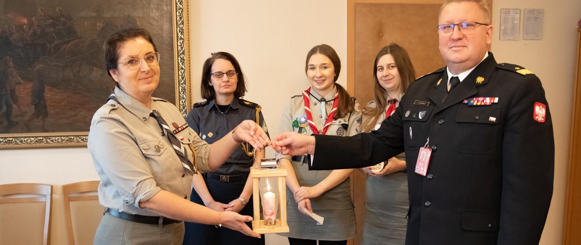 harcerka oraz komendant wojewódzki trzymają betlejemskie światło pokoju, za nimi stoją trzy harcerki