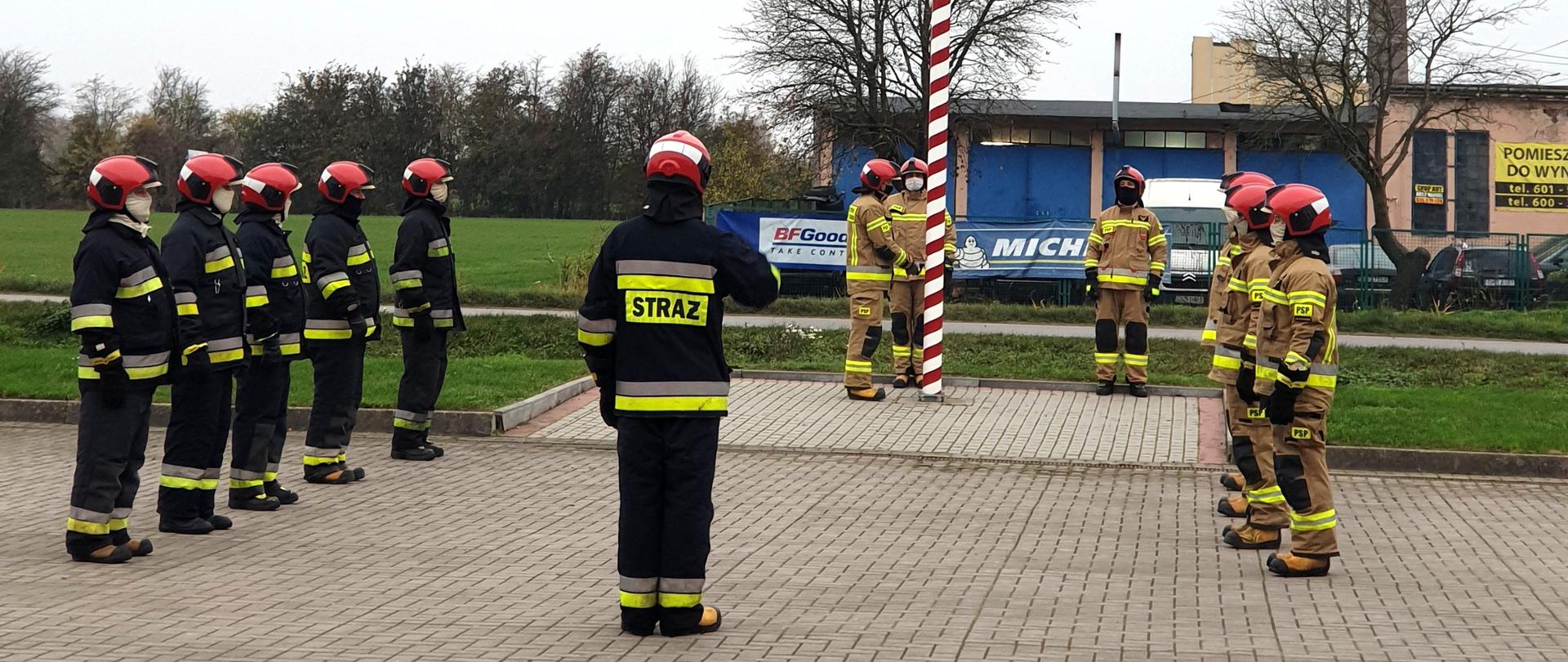 Strażacy w ubraniu bojowym podczas podnoszenia flagi na maszt.