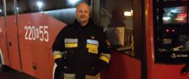 Strażak Państwowej Straży Pożarnej na tle autobusu Państwowej Straży Pożarnej