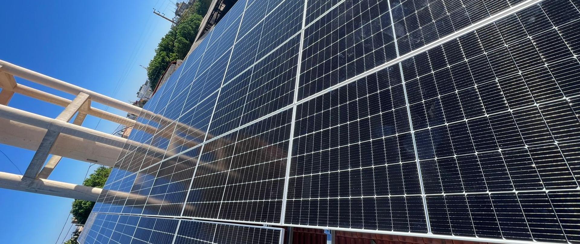 Panele fotowoltaiczne, na horyzoncie widać góry i zabudowania 