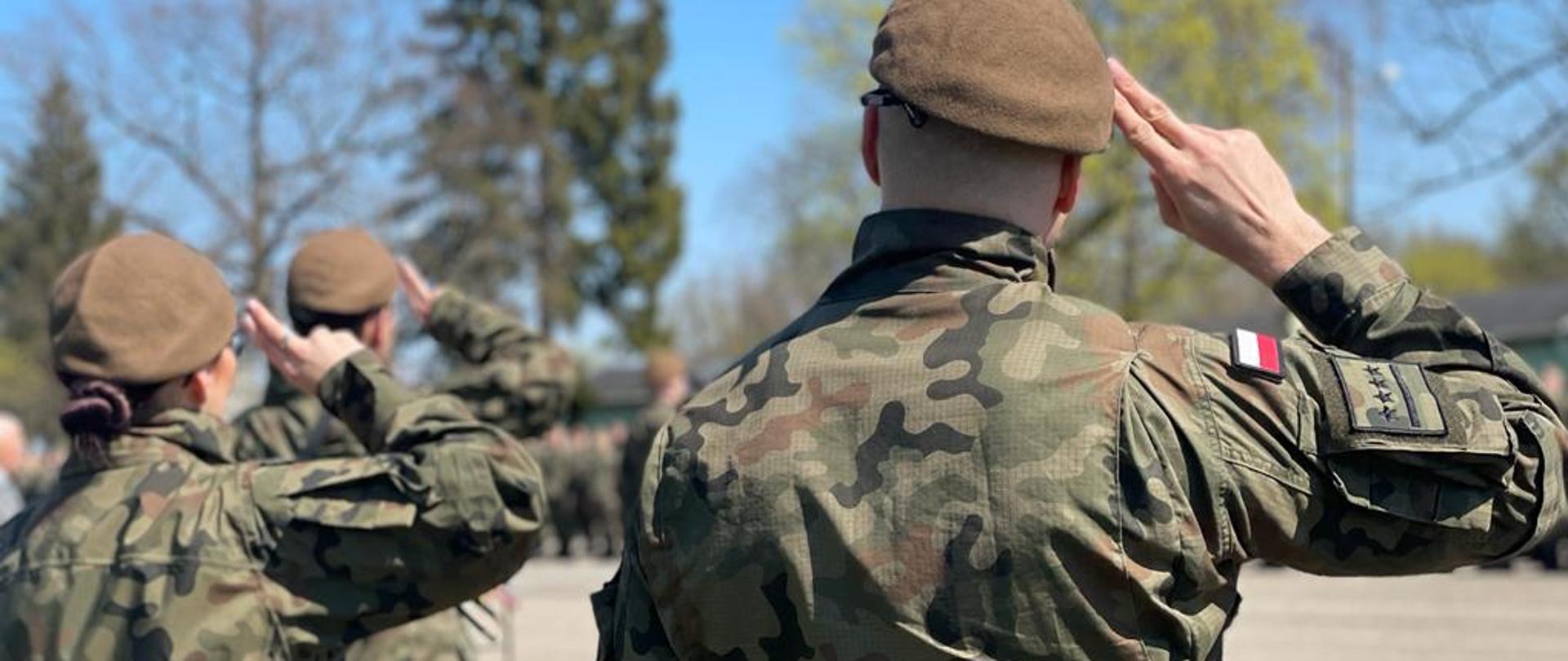 żołnierze - kobieta i dwóch mężczyzn salutujący przed polską flagą