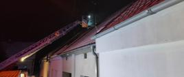 Strażak na wysięgniku drabiny mechanicznej nad dachem budynku.