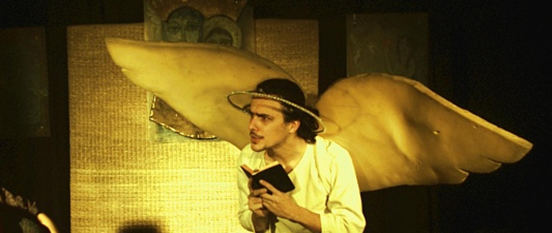 Zdjęcie przedstawia scenę z przedstawienia Pastorałka. Aktor przebrany za anioła czyta książkę 