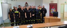 kilkunastu druhów i dwóch strażaków pozuje do zdjęcia w sali lekcyjnej po prawej od nich rollup ośrodka szkolenia KW PSP w Łodzi