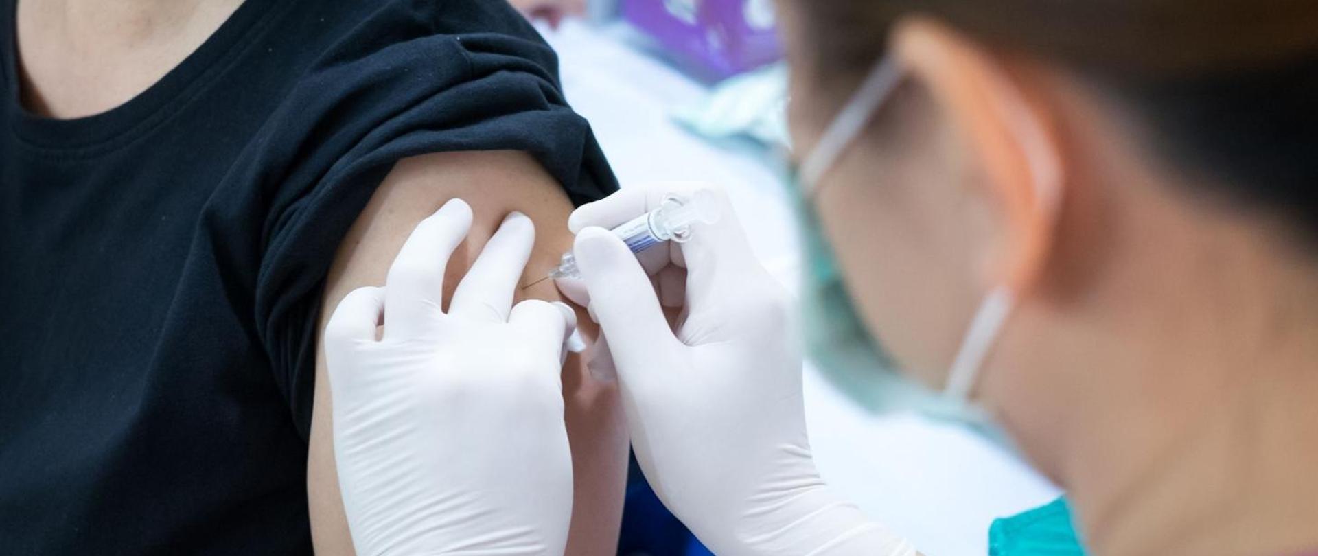 Zdjęcie przedstawia osobę przyjmującą szczepionkę w lewe ramię