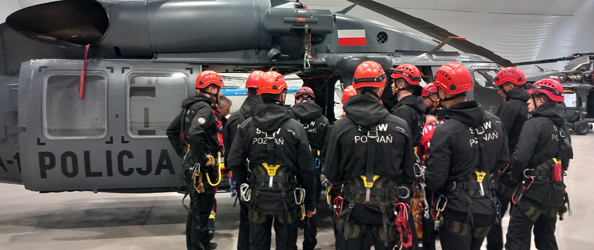 Ratownicy zgrupowani przy śmigłowcu słuchają wykładu instruktora