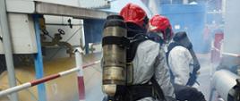 Strażacy ubrani w ubrania przeciwchemiczne aparaty ochrony dróg oddechowych niosą manekina w zadymieniu