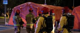 Zdjęcie przedstawia strażaków przy namiotach pneumatycznych wykorzystywanych podczas ćwiczeń do segregacji i dekontaminacji osób skażonych w wyniku zaistniałego zdarzenia
