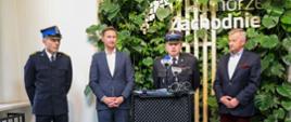 Zdjęcie przedstawia mówiącego do mikrofonu Komendanta Powiatowego PSP Białogard. Po jego bokach stoją Marszałek oraz Członek Zarządu Województwa Zachodniopomorskiego. Po lewej stronie zdjęcia stoi strażak również w galowym ubraniu