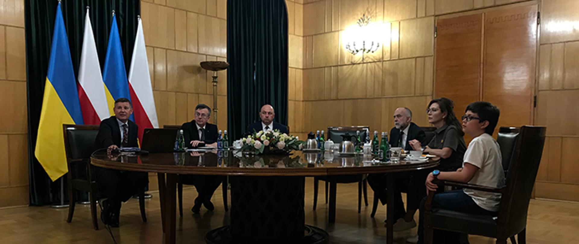 Uczestnicy spotkania siedzą przy okrągłym stole. Na jednej ze ścian flagi Polski i Ukrainy