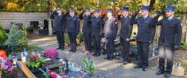 Zdjęcie przedstawia strażaków Państwowej Straży Pożarnej oddających honor na cmentarzu, przy grobie strażaka.