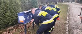 Pochyleni strażacy wrzucają ulotki do skrzynek na listy
