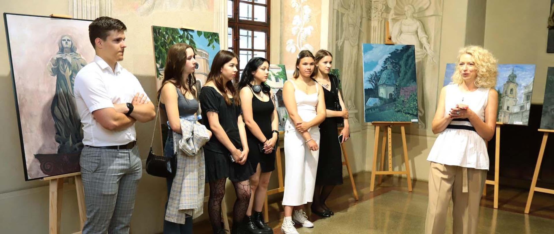 Zdjęcie przedstawia atrium Klasztoru oo. Dominikanów w Jarosławiu gdzie w centralnej części zdjęcia znajdują się uczniowie i nauczyciele szkoły biorący udział w otwarciu wernisażu. W tle zdjęcia są widoczne sztalugi z obrazami.
