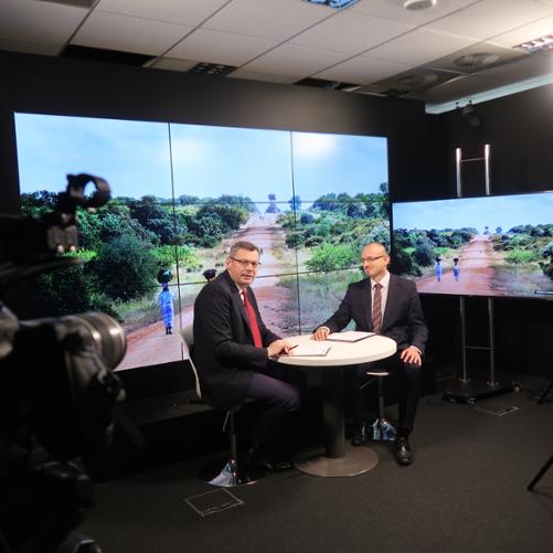 Wywiad - dwóch mężczyzn siedziacych przy stoliku, w tle zdjęcie z Afryki