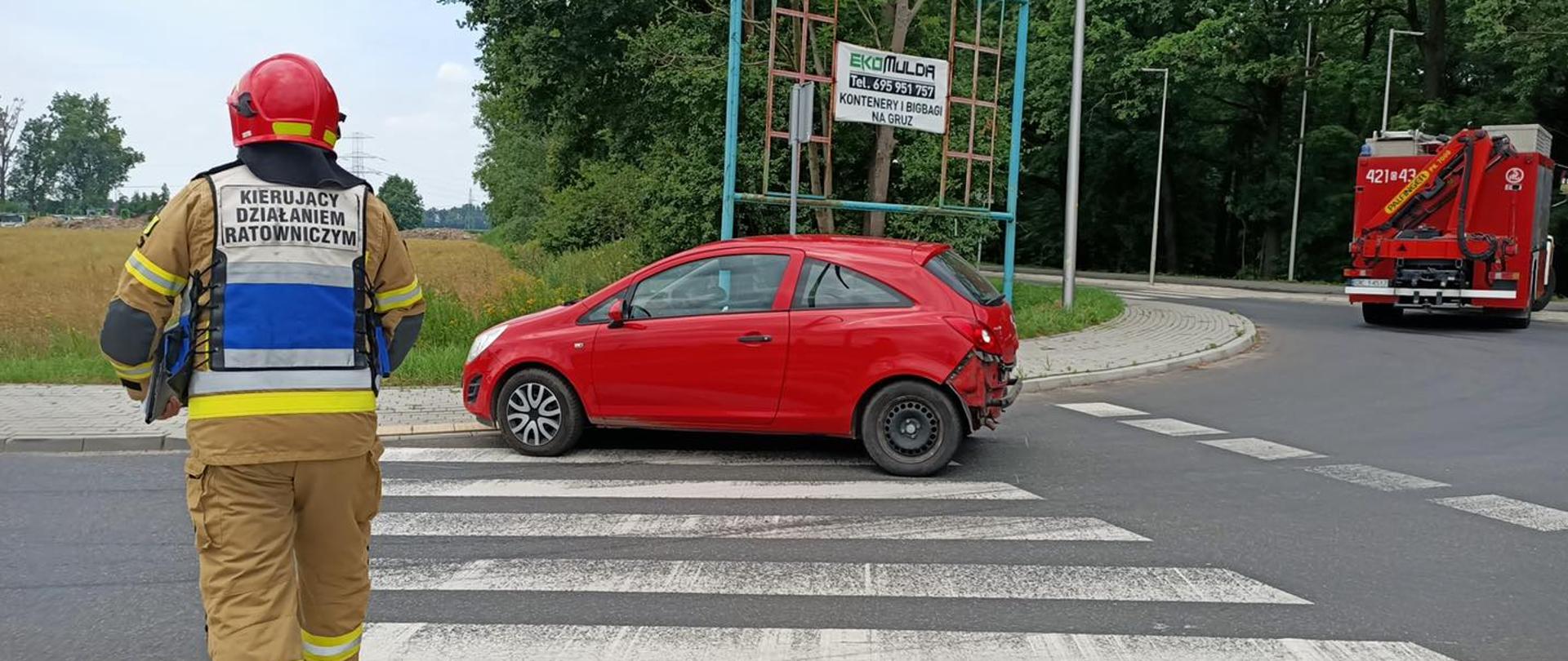 Strażak w tle czerwony samochód osobowy oraz samochód straży pożarnej