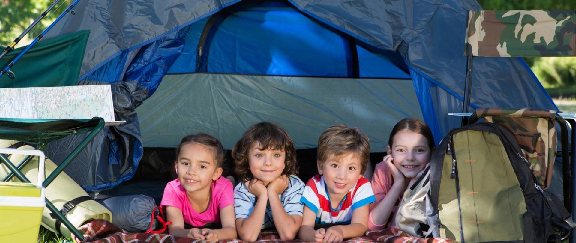 Zdjęcie czwórki uśmiechniętych dzieci leżących w namiocie, namiot koloru niebieskiego