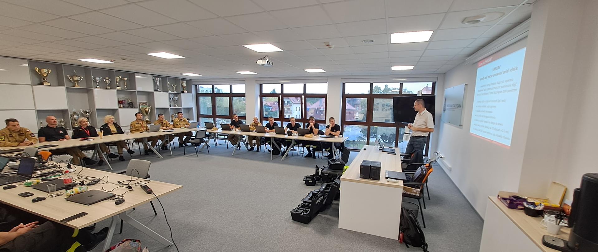 Strażacy stoją na sali szkoleniowej.