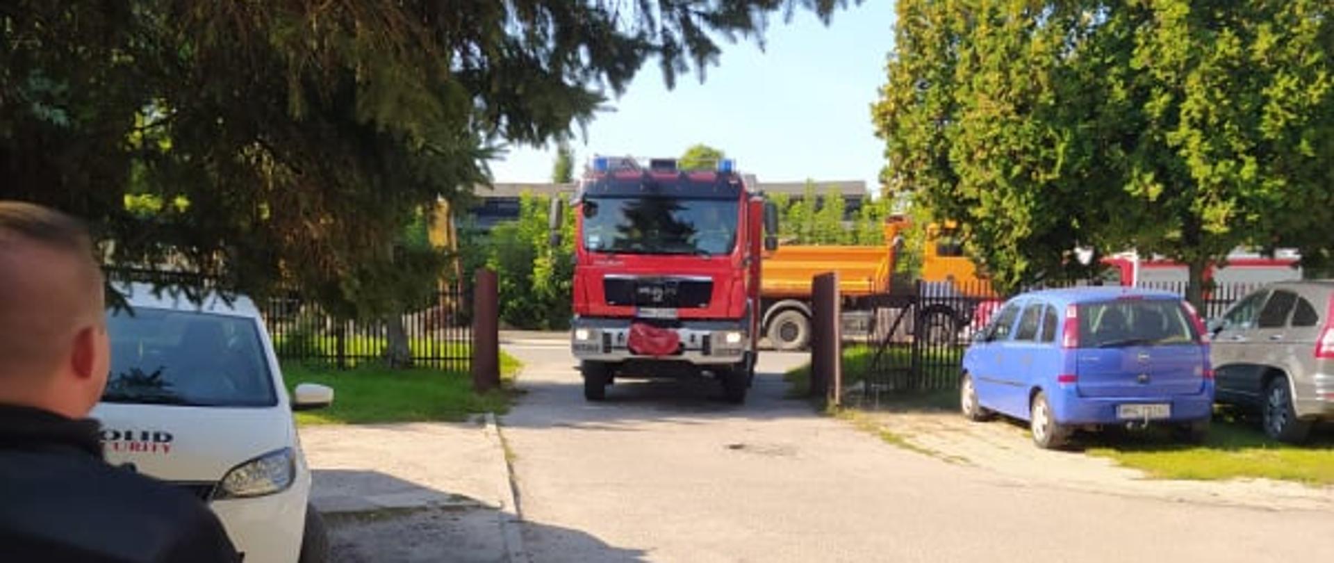 Samochód strażacki wjeżdża na plac przed budynkiem.