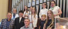 Pamiątkowe zdjęcie uczestników koncertu organowego w kościele parafialnym Najświętszego Serca Pana Jezusa w Gdyni. Na fotografii uczniowie szkół muzycznych wraz z pedagogami pozują na tle prospektu organowego; część uczestników trzyma instrumenty – oboje i trąbkę.