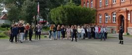 Zdjęcie przedstawia plac przed budynkiem z czerwonej cegły - Zespołem Szkół imienia Władysława Broniewskiego w Świdwinie na którym zgromadziła się młodzież. Strażak bacznie obserwuję realizację ewakuacji.