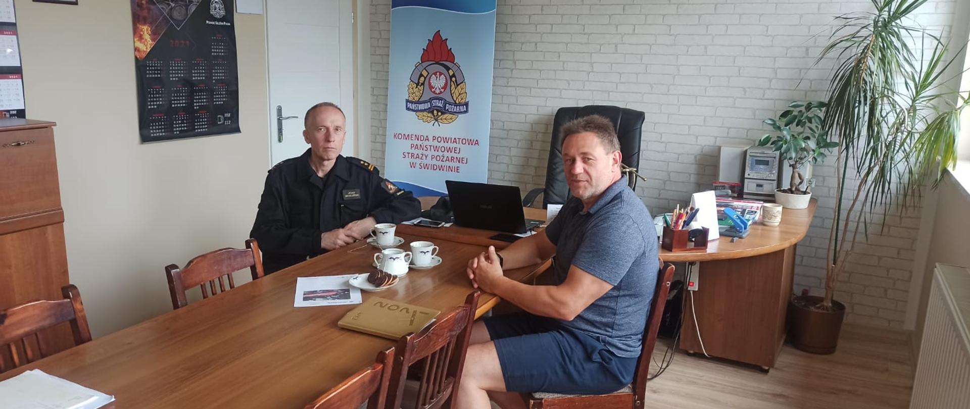 Zdjęcie przedstawia dwóch mężczyzn siedzących przy biurku podczas rozmowy.