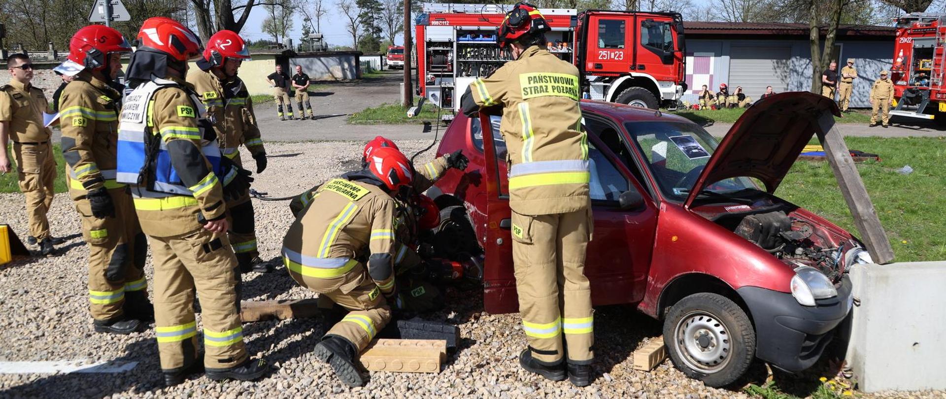 Poligon Centralnej Szkoły PSP, ćwiczący strażacy pod nadzorem instruktora prowadzą działania przy rozbitym samochodzie osobowym