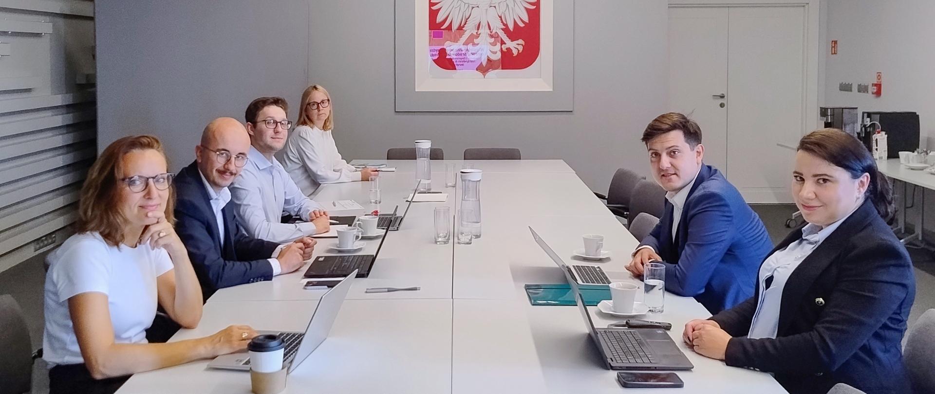 Sześć osób siedzi przy stole konferencyjnym i uśmiecha się, pozując do zdjęcia