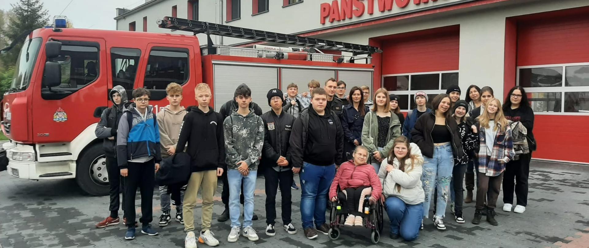 Na zdjęciu znajduje się młodzież na wspólnym zdjęciu na tle Komendy Powiatowej PSP w Chełmnie.